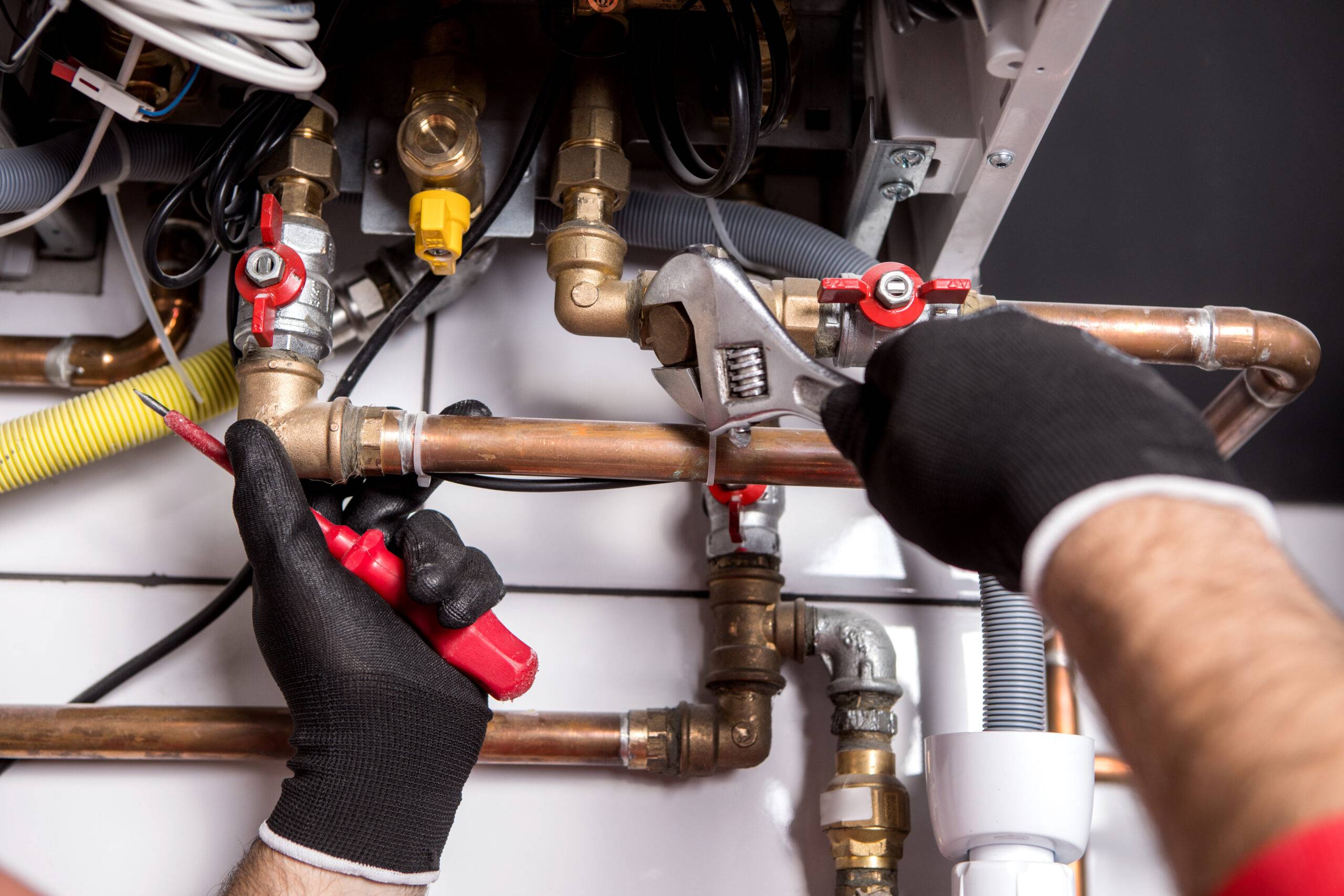 Installateur führt Wartung, Reparatur an einem Gasbrennwertgerät durch. Es sind nur die Hände sichtbar.