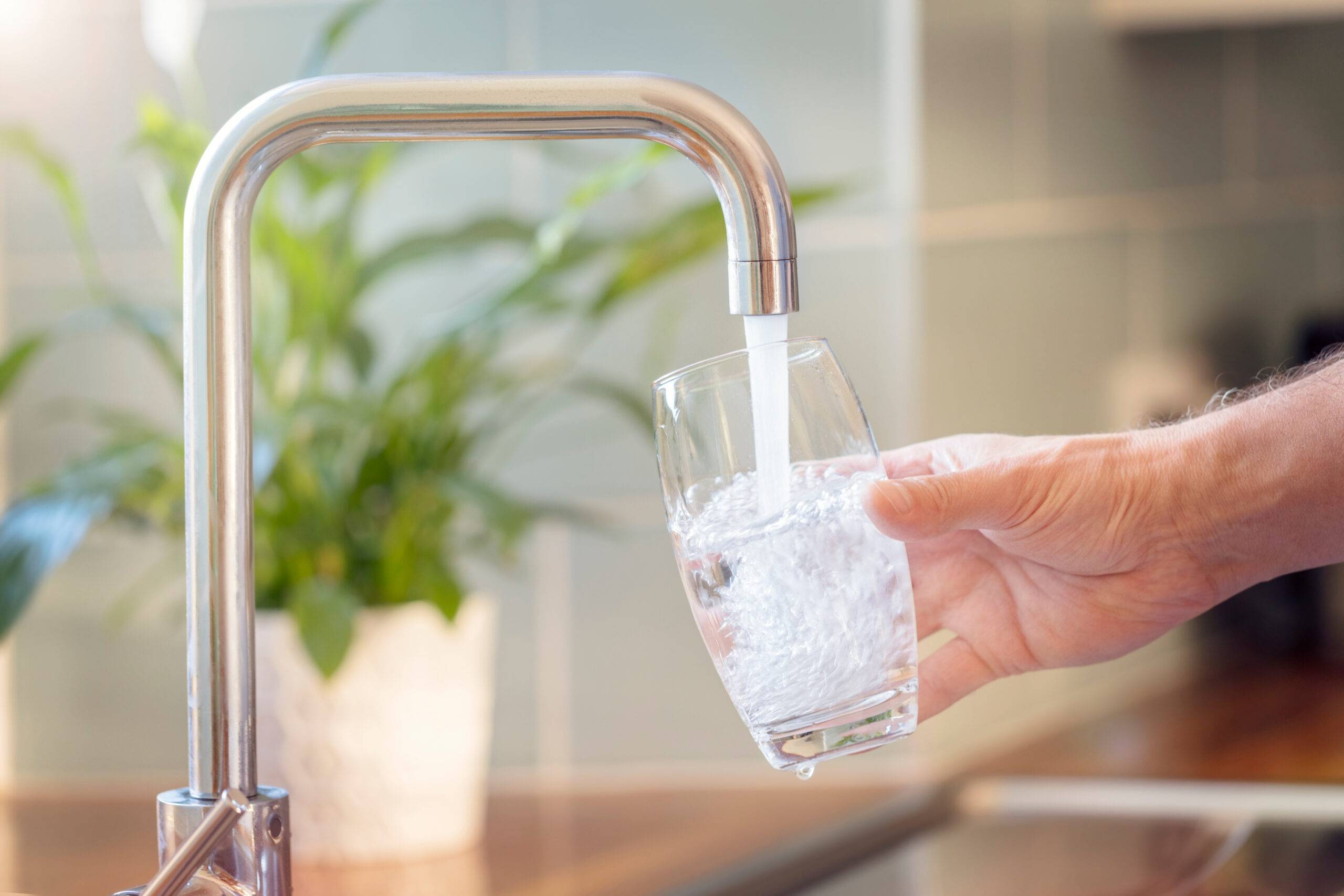 Hand hält Glas unter Wasserhahn und lässt frisches Trinkwasser einlaufen